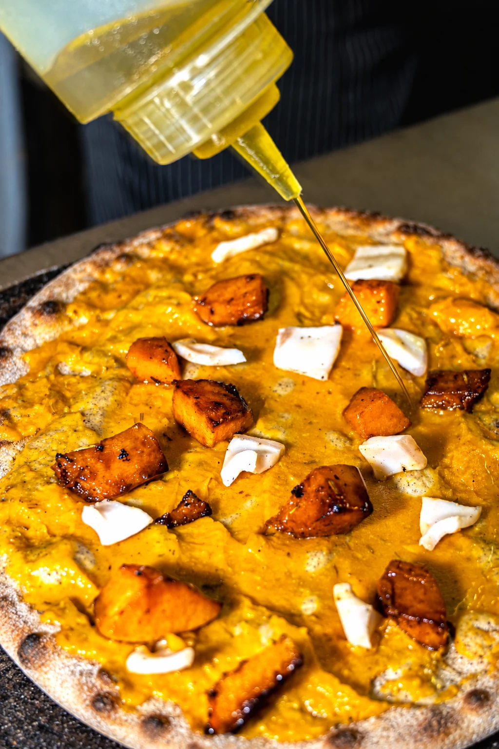 Un filo d’olio sulla pizza tonda con zucca e formaggio