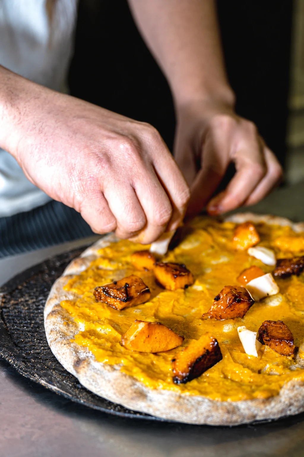 Mani del pizzaiolo che aggiungono il condimento a una pizza tonda con zucca